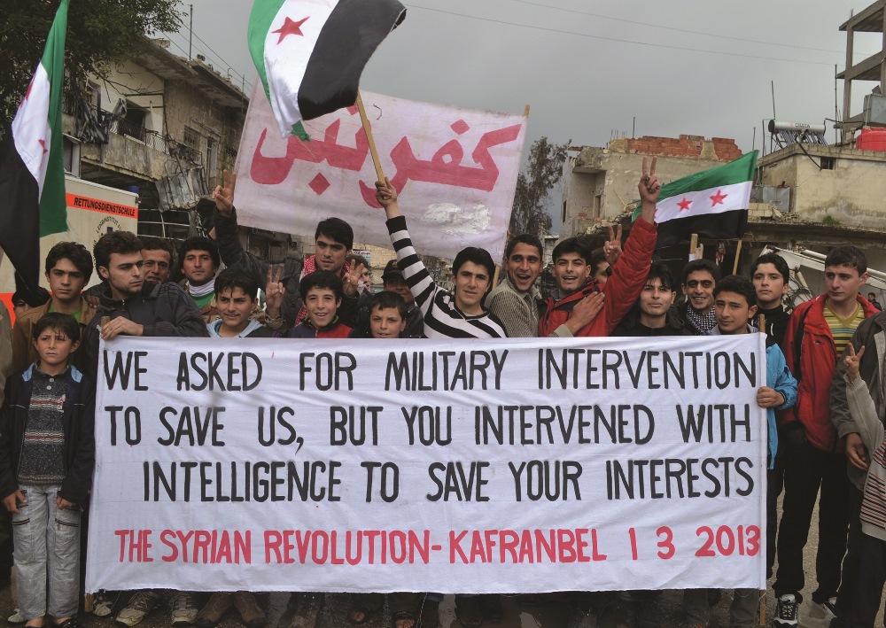 A handout picture shows Syrian anti-government protesters holding a banner against the international community’s reluctance to arm rebel forces. HO / SHAAM NEWS NETWORK / AFP